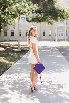 a woman in a white dress is holding a purple purse and smiling at the camera