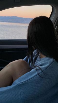 a woman sitting in the passenger seat of a car looking out at water and mountains