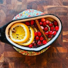 a bowl filled with oranges and cranberries on top of a wooden table