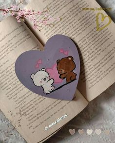 an open book with a heart shaped paper cut out of it and two bears on the pages