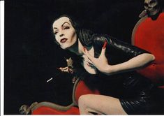 a woman dressed in black and white is sitting on a red chair with her hands behind her back