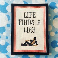 a cross stitch picture with the words life finds a way on it and a woman laying down