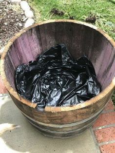 a wooden barrel filled with black trash sitting on top of a brick floor next to grass