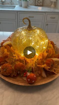 a yellow glass pumpkin sitting on top of a wooden platter filled with leaves and flowers