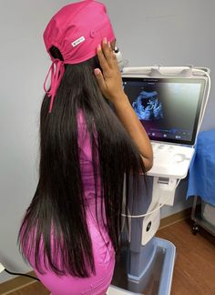 a woman with long black hair sitting in front of a computer monitor wearing a pink hat