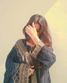 a woman covers her face with her hands while standing in front of a white wall