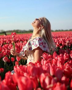 a woman standing in a field full of red tulips with her eyes closed