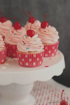 cupcakes with pink frosting and cherries are on a cake platter