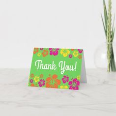 a green thank card with pink and orange flowers on it, sitting next to a plant