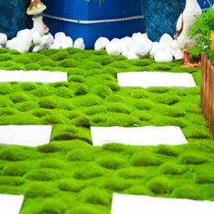 fake grass is laid out on the ground in front of potted plants and flowers