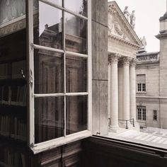 an open window with books on the windowsill in front of some old buildings and columns