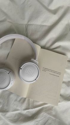 an open book and two white headphones on a bed