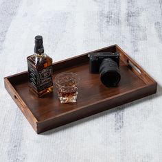 a wooden tray with a camera, glass and bottle sitting on top of the tray