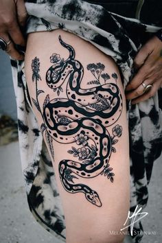 a woman's thigh with a snake tattoo on her leg and flowers around it