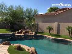 a pool with artificial grass and rocks in the back yard, next to a house