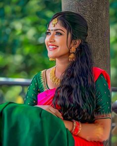 a woman in a red and green sari sitting next to a tree with her arms crossed