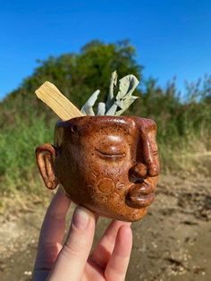 a hand holding up a clay head with plants growing out of it's face