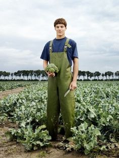 a young man standing in a field holding vegetables