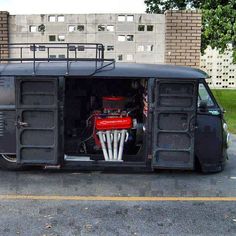 an old black bus is parked in a parking lot with its doors open and the engine visible