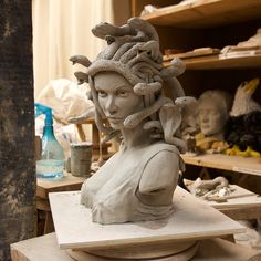 a clay sculpture of a woman's head with snakes in her hair, sitting on a workbench