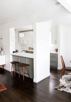 an open kitchen and dining room with white walls, wood flooring and wooden stools