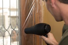 a man using a hair dryer on the side of a door with a window in the background