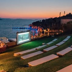 an outdoor movie is set up on the lawn next to the water at night time