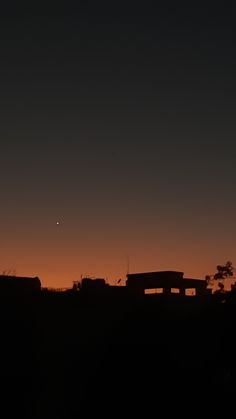 the sun is setting over some buildings in the distance with a plane flying above it