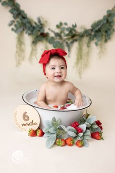 a baby sitting in a bowl with strawberries and greenery