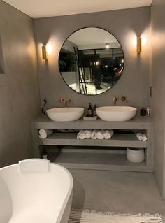 a bathroom with two sinks and a bathtub under a round mirror on the wall