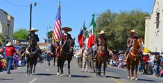 several people riding horses down the street with flags on their backs and in sombreros