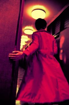 a woman in a long red dress is walking down the hallway with her hand on the door handle