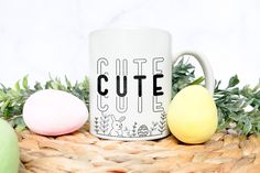 a white coffee mug sitting on top of a basket next to two colored easter eggs