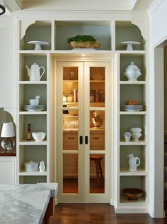 an open pantry with glass doors and shelves filled with dishes on top of each shelf