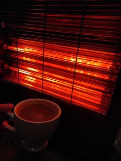 a cup of coffee sitting in front of an electric heater that is glowing red