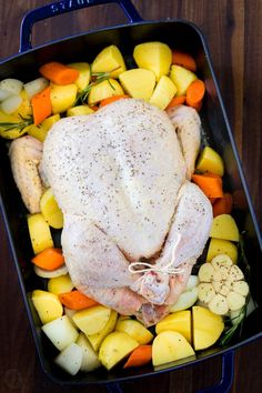 a whole chicken in a roasting pan with potatoes, carrots and other vegetables