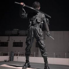 a man dressed in all black holding two swords and standing on top of a ramp