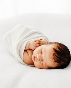 a baby wrapped in a white blanket laying on top of a bed with its eyes closed