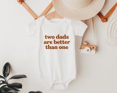 🎄🎄 Xmas deadlines: Place your order by Dec 11 for the best chance of receiving it in time for Xmas 🎄🎄 Two Dads are Better Than One Onesie® or Kids tee This super soft 100% cotton bodysuit is a perfect gift for a little cutie, a pregnancy announcement, or a gorgeous gift for two new Daddies!  The Details: * Super soft and comfy!  * Lightweight and breathable * 100% cotton for the softest feel imaginable * The design is printed directly on the garment, no vinyl or stencils - which means it will last through many washes * Size details in photos. If you're not sure on size, I always recommend ordering a size up! Kids can always grow into a bigger size Production + Shipping: Your item is custom printed to order within 2-7 business days. See your shipping speed at checkout. Don't hesitate to Casual Cotton Bodysuit With Letter Print, Father's Day Cotton Onesie With Graphic Print, Mother's Day Cotton Bodysuit With Letter Print, White Cotton Bodysuit With Graphic Print, White Cotton Bodysuit With Letter Print, Mother's Day White Letter Print Bodysuit, Pride Ideas, Rainbow Family, Gay Dads