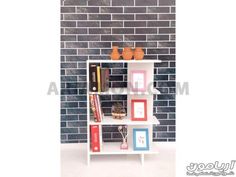 a white book shelf with books and pictures on the top, in front of a brick wall