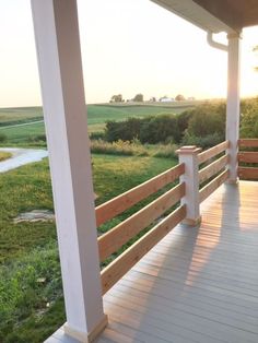 a porch with wooden railings and grass on the other side, looking out over an open field