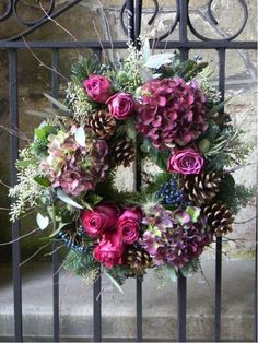 a wreath made out of flowers and pine cones on a gated in area with stone walls