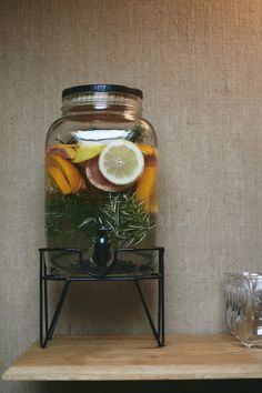 a glass jar filled with water and lemon slices on top of a wooden shelf next to glasses