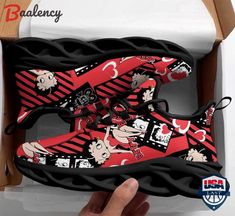 someone is holding up a pair of red and black sneakers with cartoon characters on them