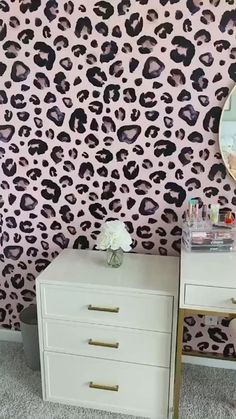 a white dresser sitting next to a mirror on top of a wall covered in leopard print