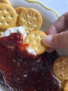 a person is picking up crackers from a plate of jelly cheese and crackers