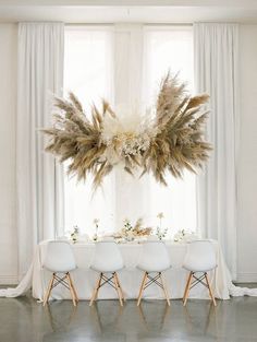 the table is set with white chairs and tall pamodia centerpiece on top