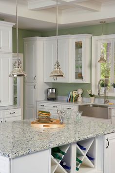 a kitchen with white cabinets and marble counter tops, an island in the middle has wine glasses on it