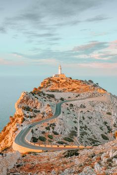 a winding road on the side of a mountain with a light house in the distance