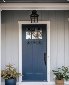 a blue front door with two potted plants on the side and a light fixture above it